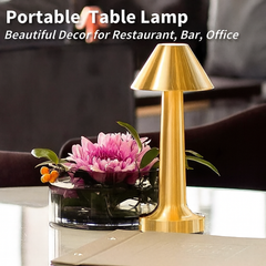 Portable gold table lamp on restaurant table beside pink flower centerpiece
