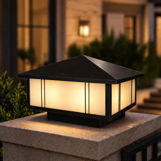 Decorative outdoor light fixture on a stone pedestal with a blurred house and garden in the background.