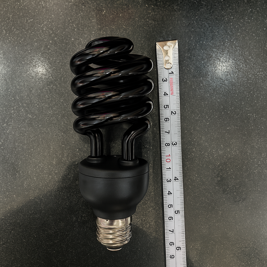 Black spiral light bulb next to a ruler on a dark surface