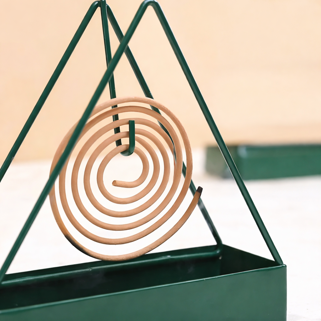 Coil of incense hanging from a green metal stand against a beige background