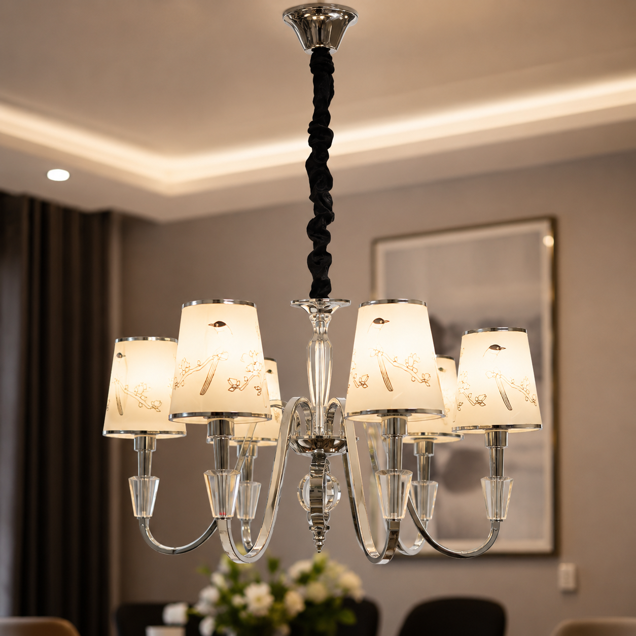 Chandelier hanging in a room with a mirror and flowers on a table.