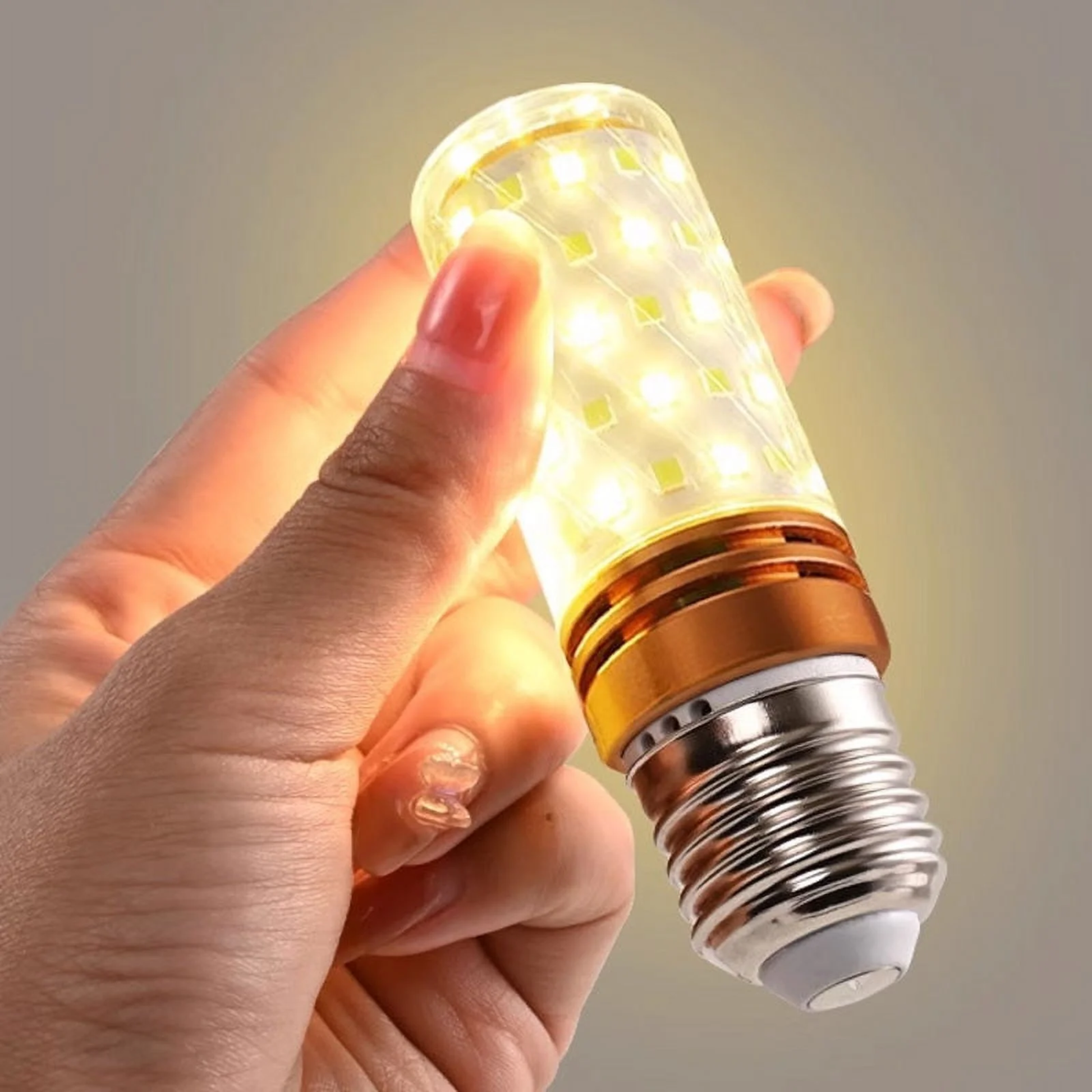 Hand holding a LED light bulb with a warm glow against a neutral background
