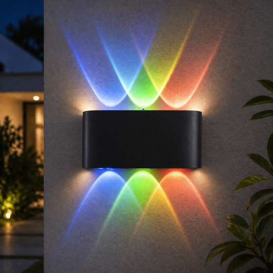 Black outdoor wall light fixture casting colorful beams on a wall with plants and house in the background.
