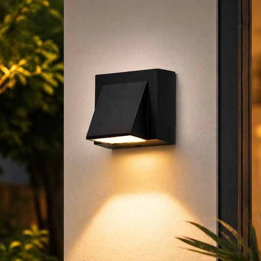 Black outdoor wall light fixture on a building exterior with plants around.